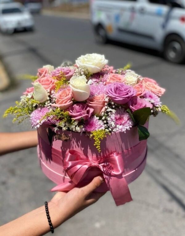 Caja circular con rosas en tonos pastel con lilas y follaje mixto